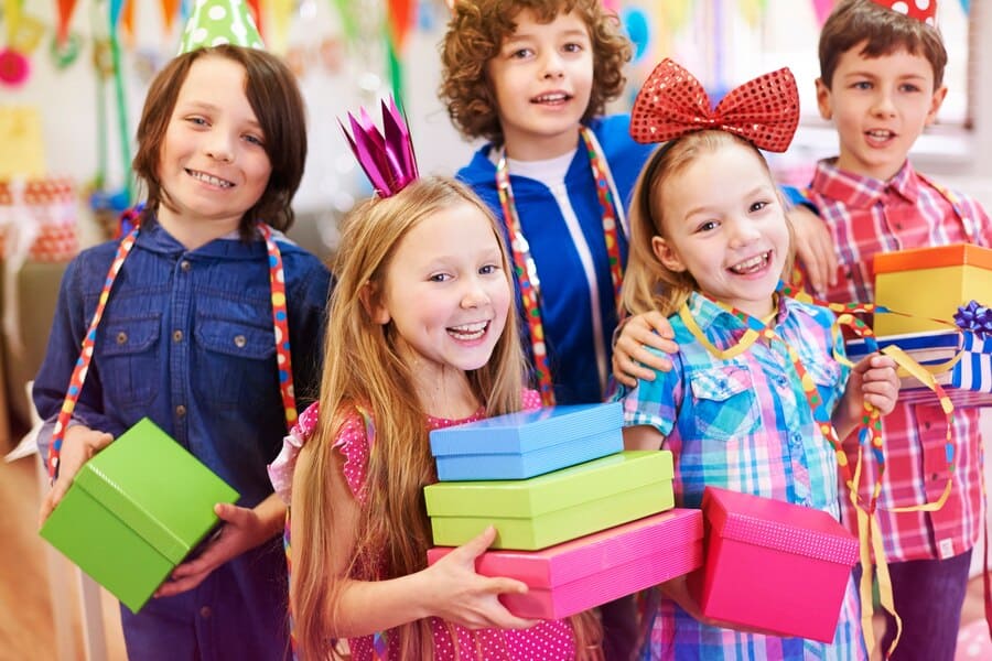 Children excitedly hold colorful birthday gifts in a festive party room decorated for a Magic Show Parties