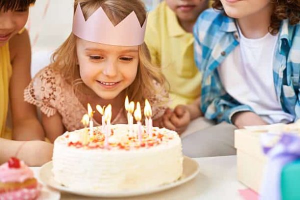 Lovely little girl and her friends looking at burning birthday candles